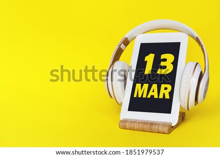 March 13rd. Day 13 of month, Calendar date. Stylish headphones and modern tablet on yellow background. Space for text. Concept education, technology, lifestyle. Spring month, day of the year concept