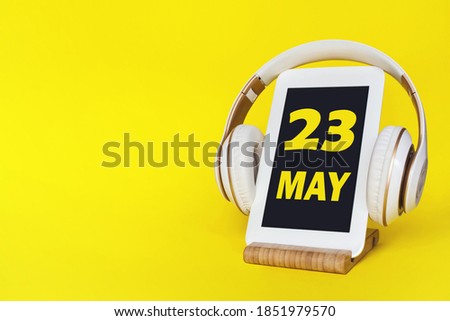 May 23rd. Day 23 of month, Calendar date. Stylish headphones and modern tablet on yellow background. Space for text. Concept education, technology, lifestyle. Spring month, day of the year concept