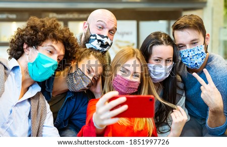 smiling group of people wearing protective face mask posing for a picture together in front of a smartphone. happy social influencers taking a selfie pic together. concept about new normal lifestyle