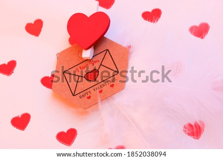 Brown envelope with a love note for a loved one on Valentine's Day, the inscription I love you on the background of gift paper with little red hearts, and white feathers.
