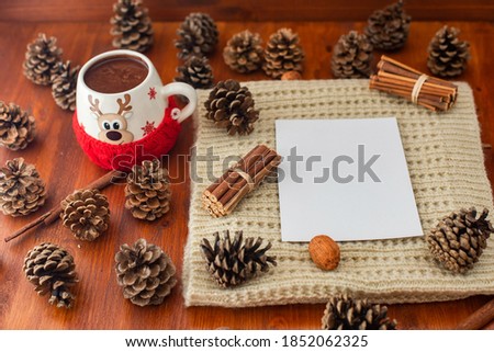 Christmas background. pine cones and green needles. plain white sheet of paper. knitted gray sweater. cup of hot cocoa. wood table.