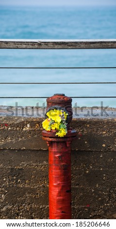 Red grungy hydrant on the old stone pier with colorful bouquet and sea at backgrounds. Romance background. Romantic honeymoon vacation idea.