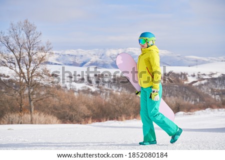 Woman with snowboard against background of mountains in winter