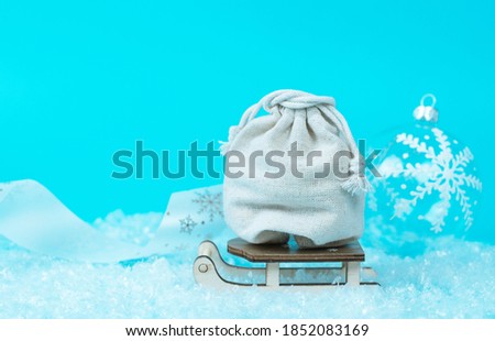 canvas bag with Christmas gifts in a wooden sleigh on snow and blue background, concept of delivery for Christmas and New year