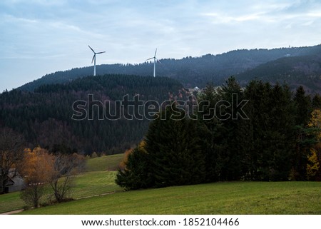 Deciduous and coniferous forest on the hill disappears in the autumn fog, wind mills and clouds. Landscape from Germany, Schwartzwald. Colorful travel background