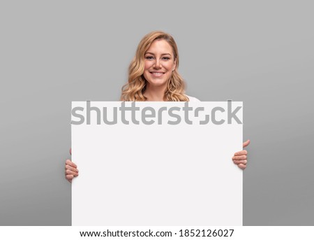 Young woman holding a large white blank sheet on a gray background.
