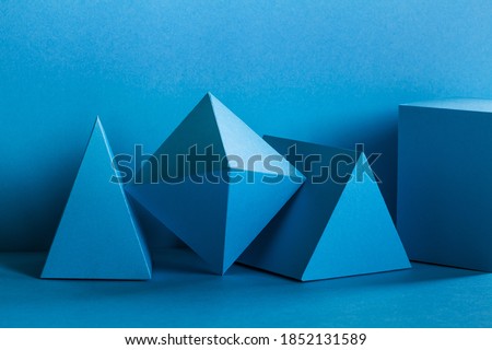 Abstract geometrical figures still life composition. Three-dimensional prism pyramid rectangular cube objects on turquoise background. Platonic solids figures,  selective focus.