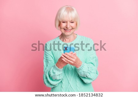 Photo portrait of cheerful old lady keeping smartphone smiling wearing teal knitted sweater isolated on pastel pink color background