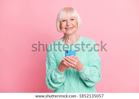 Photo portrait of cheerful old lady using mobile phone smiling typing message isolated on pastel pink color background