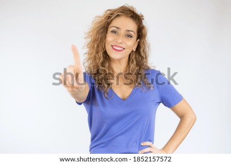 Smiling woman in casual clothes pointing up and looking at the camera over white background
