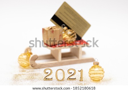 Golden wooden numbers 2021 with two christmas balls and golden credit card on santa Claus slide against white background, empty space