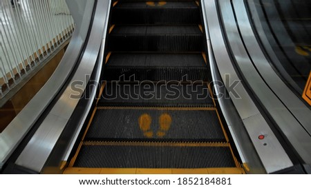 Black staircase escolator in a shopping center with a footprint sign for keeping a social distance
