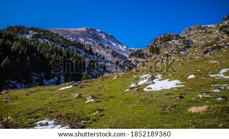 Autumn picture of Pyrenean peaks overlooking the Vall de Nuria, Catalonia, Spain, in sunny day, blue sky, green grass, snow-capped summits 