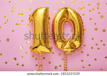 10 air balloon numbers on pink background. 10 k gold foil balloons with confetti. Birthday party flat lay with copy space Royalty-Free Stock Photo #1852215529