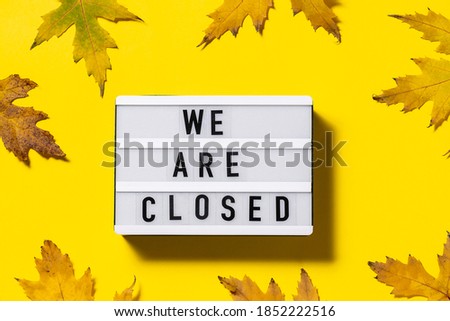 Text We are closed on the lightbox on bright yellow background with maple leaves. Concept of autumn lockdown and quarantine. 