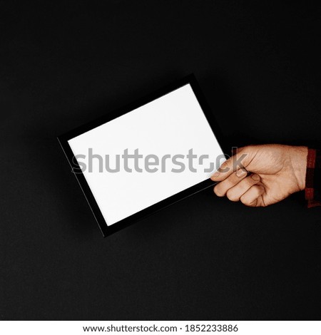 Photo frame in hands on black background. Preparation for text, mockup, copy space.