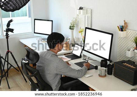 Graphic designer or photographer is working with empty screen computer and digital tablet at his workspace.