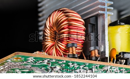Ferrite core inductors wrapped with copper wire on black background. Electronic toroid and solenoid coils. Passive electrical components soldered on bottom side of circuit board detail. Alu heat sink. Royalty-Free Stock Photo #1852244104