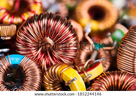 Toroidal electronic inductors on heap in electrotechnical background. Closeup of beautiful induction coils with copper wire winding on magnetic ferrite core. Colored electrical engineering components. Royalty-Free Stock Photo #1852244146