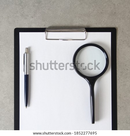 Template of white paper with a ballpoint pen and magnifying glass on light grey concrete background in a black tablet with a clip. Concept of new idea, business plan and strategy, development and