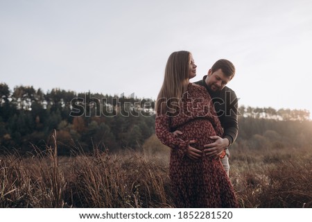 Happy and young pregnant couple hugging in nature