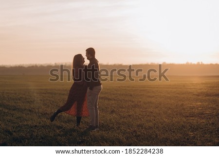 Husband and his pregnant wife are walking at sunset in field on the outside
