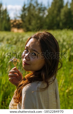 A vertical shot of a beautiful young Asian lady in a park holding a flower in her hand