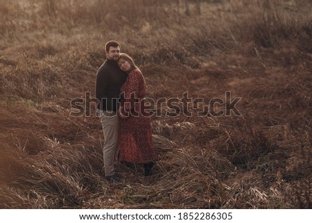 Beautiful pregnant woman and her husband hugging belly on nature background. Autumn landscape.