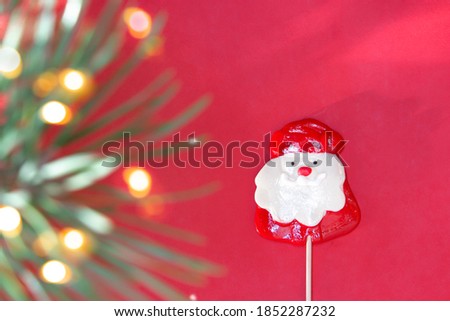 Red creative abstract cover design with Lollipop Santa Claus caramel and blurred pine branches with bokeh effect. Template for postcards, posts, and promotions. Copy space. Flat lay