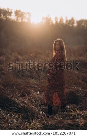 Pregnant woman standing in a golden field with dry grass at sunset.