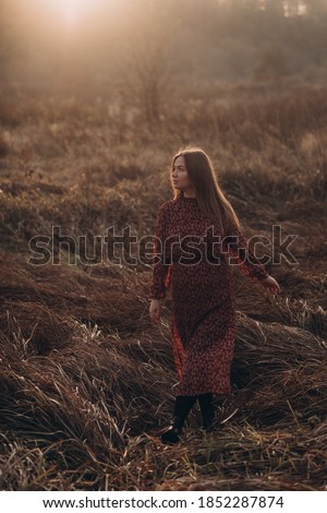 Pregnant woman standing in a golden field with dry grass at sunset.