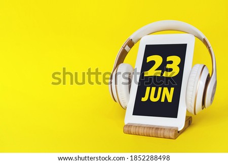 June 23rd. Day 23 of month, Calendar date. Stylish headphones and modern tablet on yellow background. Space for text. Education, technology, lifestyle. Summer month, day of the year concept