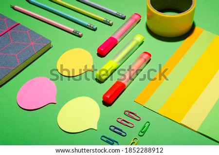 Colorful office stationery on the green background.Notes, markers, paper, tape, notebook and pencils