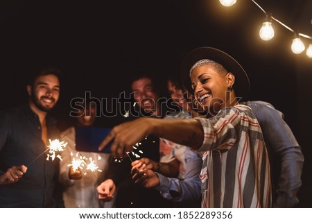 Happy young friends celebrating new year eve with sparklers fireworks while taking selfie with mobile smartphone on patio house party - Youth people lifestyle and holidays concept Royalty-Free Stock Photo #1852289356