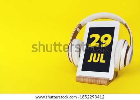 July 29th. Day2 9 of month, Calendar date. Stylish headphones and modern tablet on yellow background. Space for text. Education, technology, lifestyle. Summer month, day of the year concept