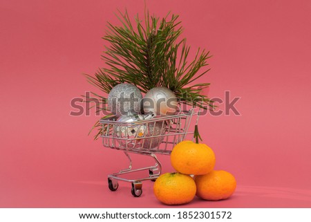 a mini-cart from a supermarket with Christmas balls and a pine branch,tangerines nearby.In theory,attributes for the New Year's holiday,delivery of any goods to your home,buying goods in online stores