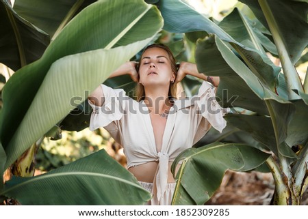 Beautiful woman in the jungle. A resort or hotel with tropical trees and plants. Woman with near banana leaf. Girl on vacation in the rainforest