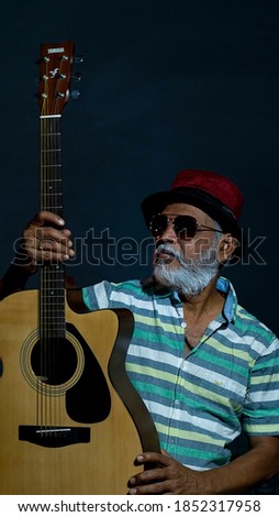 A South Asian man wearing a hat and glasses and posing with a guilting in his hands