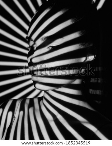 black and white portrait of woman in a shadow stripe. shadow pattern on the face and body in the form of stripes. fashion, beauty, makeup, cosmetics, beauty salon, style, personal care, poster Royalty-Free Stock Photo #1852345519