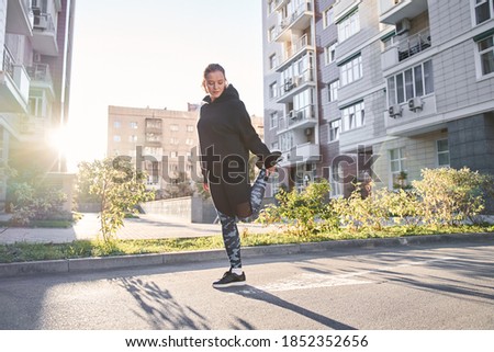 Blonde caucasian woman warming up before a morning workout near her house at the street at the morning with golden sunrise. Stock photo