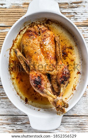 Baked whole farm duck in a baking dish. White wooden background. Top view