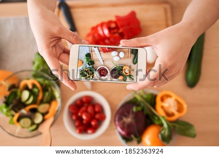 Top view of the caucasian woman taking a photo with smartphone for lunch or dinner. Woman taking picture of her salad and vegetables. Posting or sharing popular food for social media concept