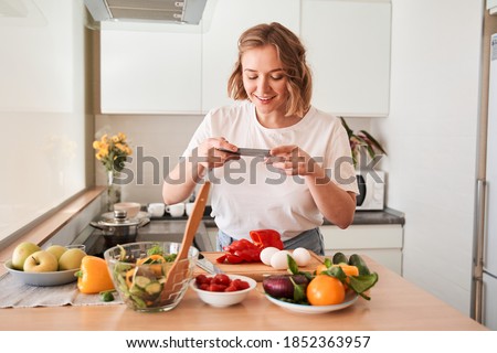 Waist up portrait of food blogger taking picture of cooked salad placing on wooden surface while standing at the kitchen. Stock photo