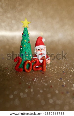 Playful clay christmas concept. Colorful handmade miniature Christmas tree and Santa Claus in gold background. 2021 new year.