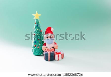 Playful clay christmas concept. Colorful handmade miniature Christmas tree, presents and Santa Claus with mask on green background.