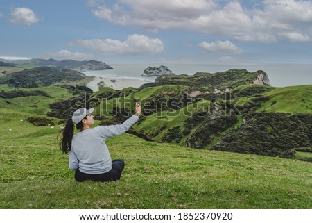 Young woman sitting on hillside on Wharariki beach view point. New Zealand.