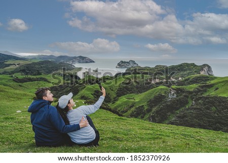 Couple taking picture at lookout above the hills in Wharariki beach, New Zealand.