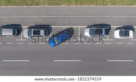 DRONE, TOP DOWN: Flying above a shiny blue car driving out of a roadside parking space. Modern vehicle leaves a parking spot in a long line of parked cars next to an empty city street in Ljubljana. Royalty-Free Stock Photo #1852374559