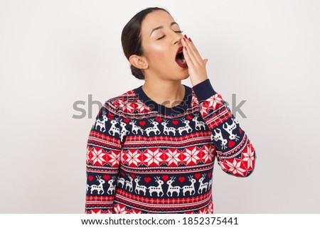 Beautiful arab girl wearing christmas sweater over isolated white background being tired and yawning after spending all day at work.