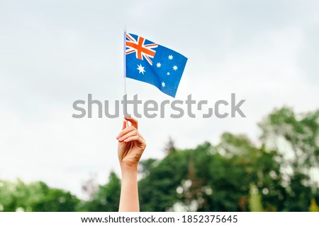 Closeup of woman human hand arm waving Australian flag against blue sky. Proud citizen man celebrating national Australia Day in January outdoor. National day holiday. Royalty-Free Stock Photo #1852375645